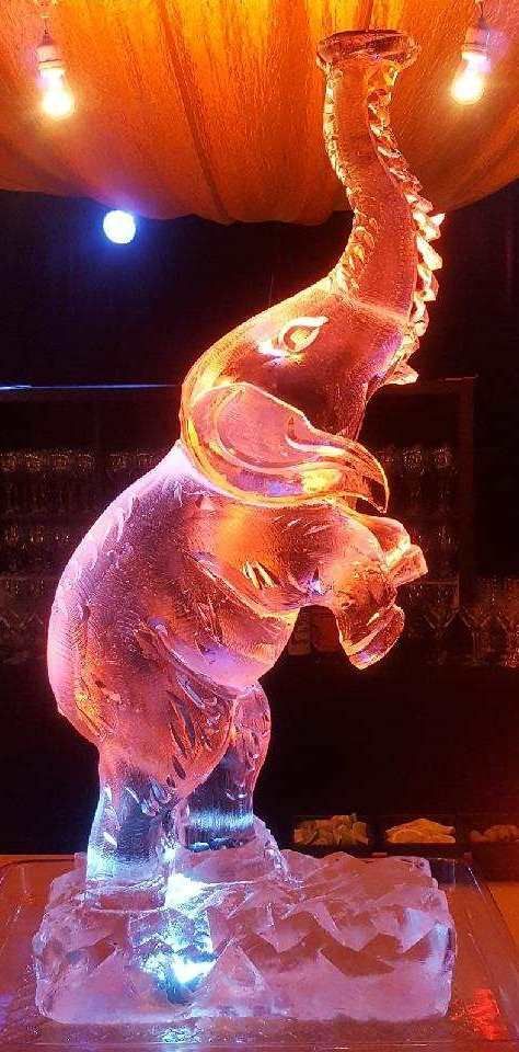 Illuminated ice sculpture of an elephant with a raised trunk on a lit stage