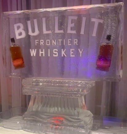 Bullet Frontier Whiskey sign lit in purple, with two hanging shot glasses on a clear display.