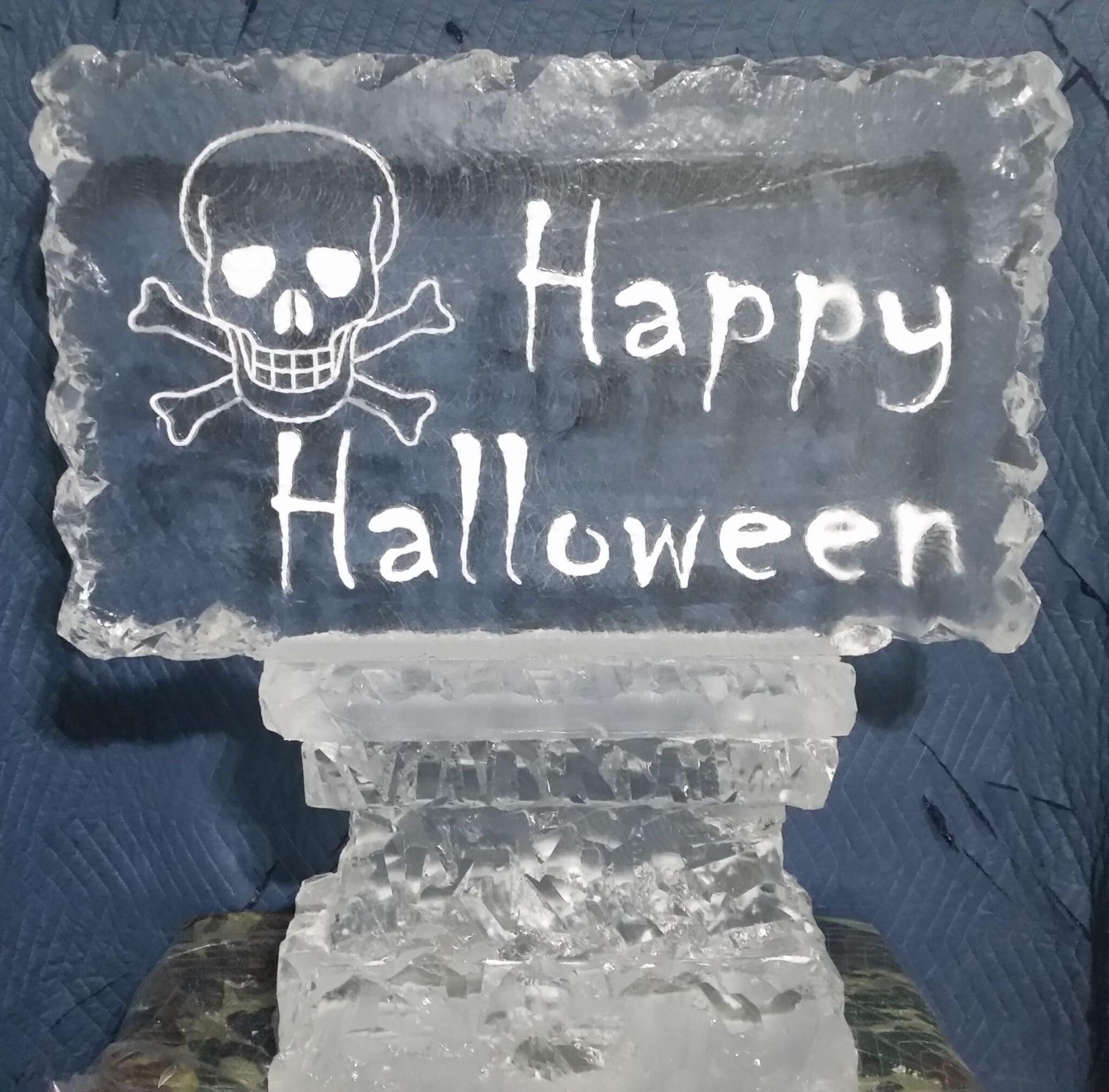 Halloween sign with skull and crossbones on a frosted plaque reading “Happy Halloween”