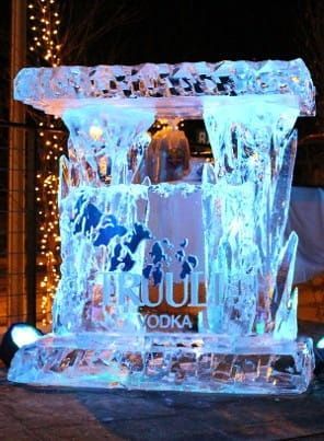 Blue ice sculpture of a vodka bottle with cascading ice, glowing in a dark setting