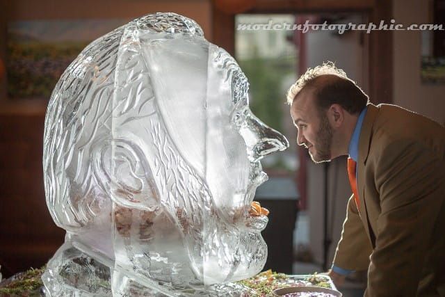 Man leans close to a large transparent ice sculpture of a face in a warmly lit room