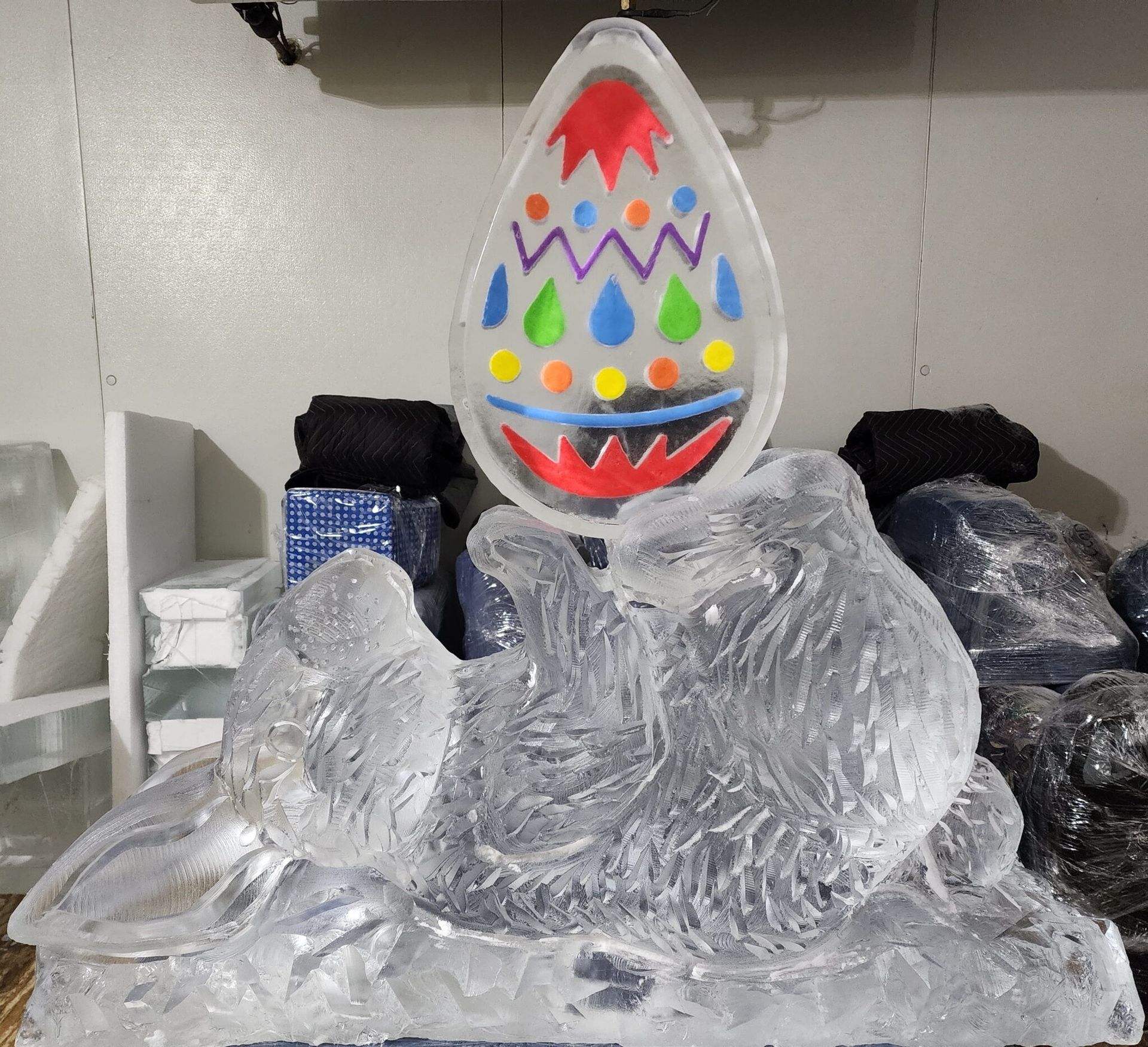 Clear glass egg sculpture with colorful dots and zigzags on a crinkled silver base outdoors