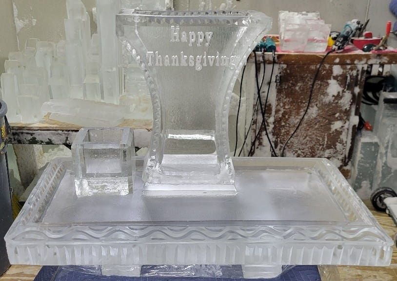 Clear ice sculpture with “Happy Thanksgiving” engraved on it, displayed on a table.