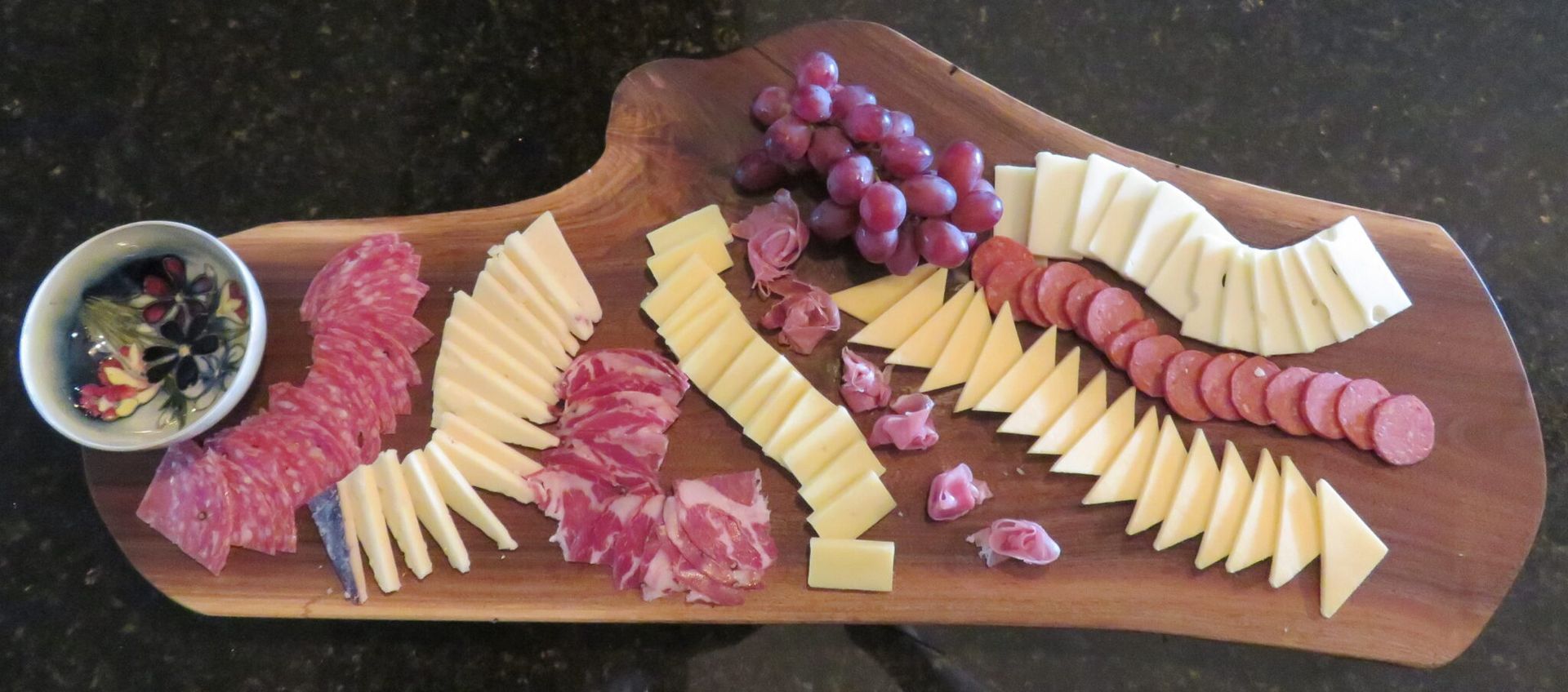 Charcuterie board with sliced meats, cheeses, grapes, crackers, and a small bowl of dip
