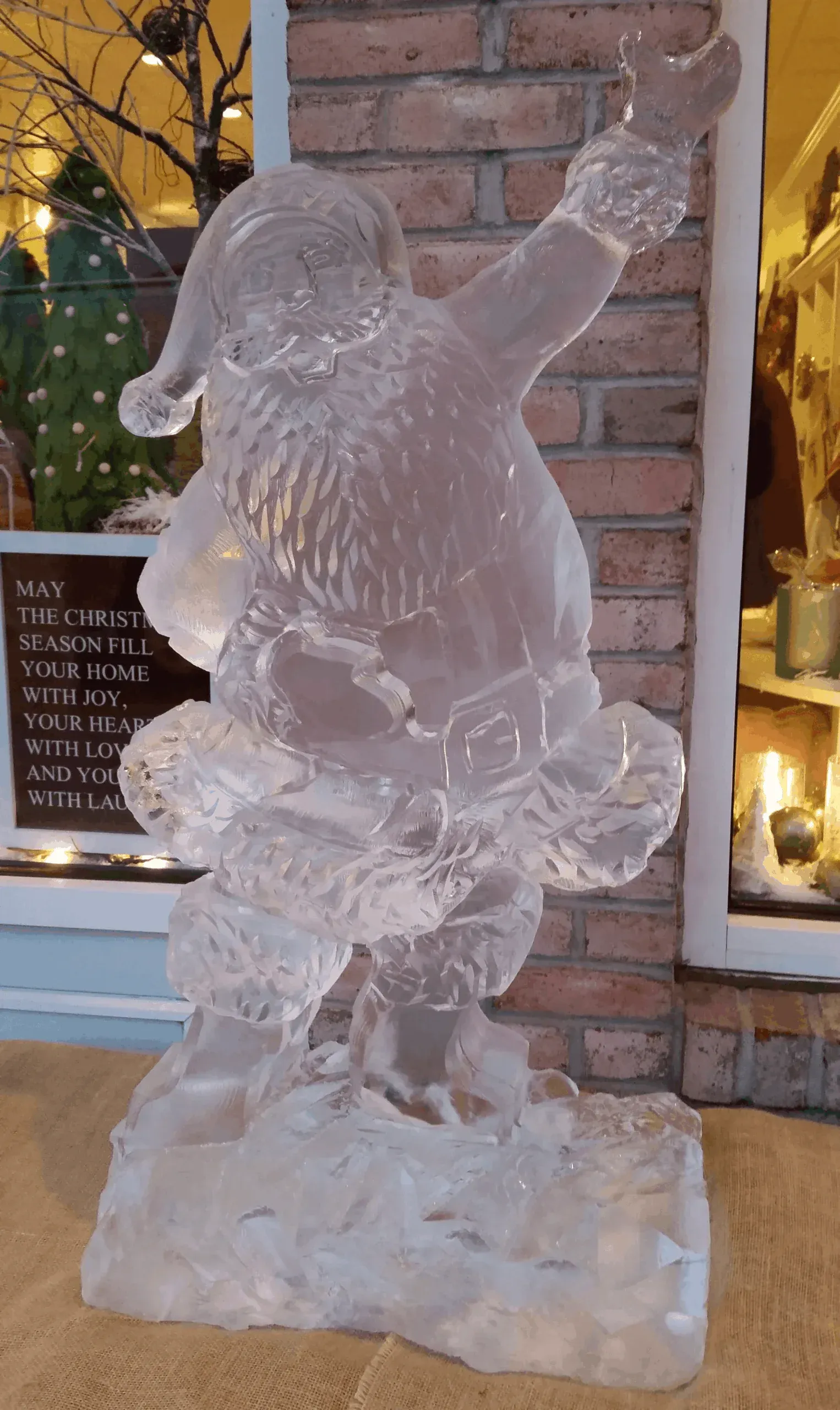 Ice sculpture of Santa Claus on a pedestal outside a brick building at night