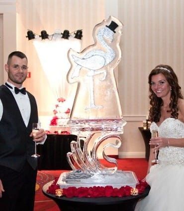 Bride and groom beside a tall ice sculpture on a red-carpeted event table