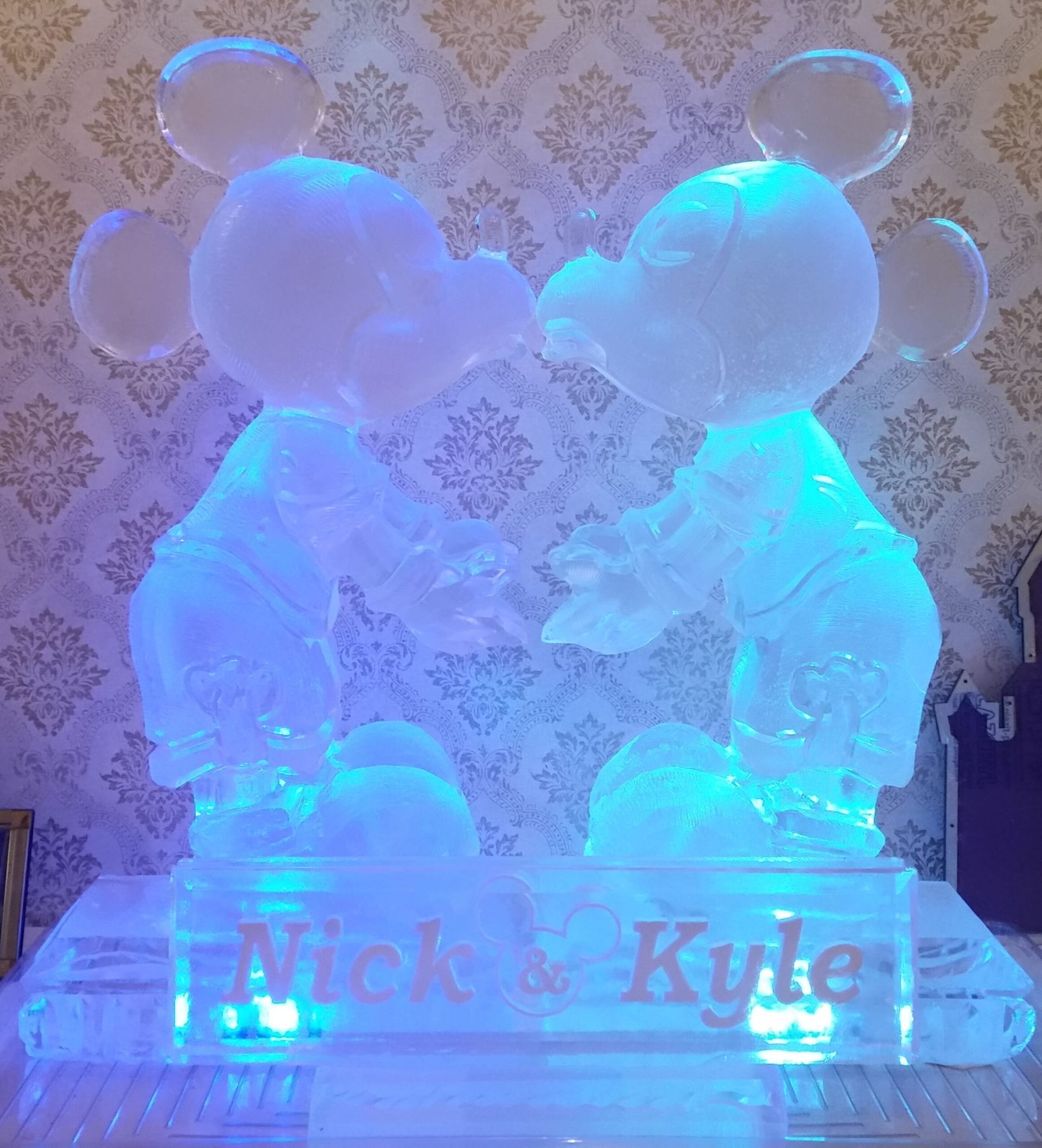 Blue-lit ice sculpture of Mickey and Minnie Mouse with “Nick & Kyle” engraved at the base