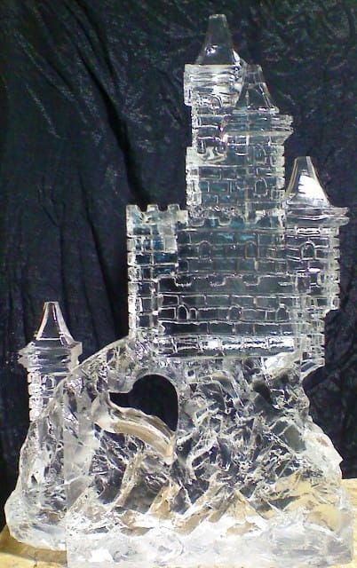 Clear crystal castle sculpture on a dark background, with a smaller tower and arched opening at the base