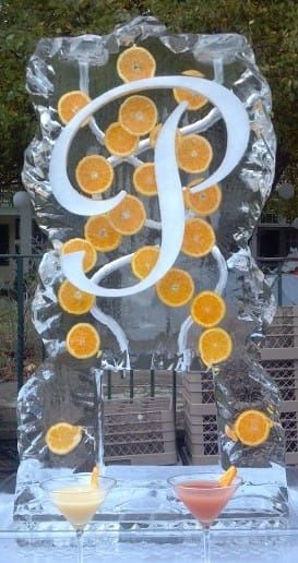 Clear ice sculpture with a white monogram and embedded orange slices, standing on a table.