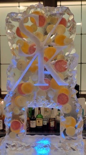 White arch display with orange and yellow ornaments and a large white letter A, lit by blue light at the base.