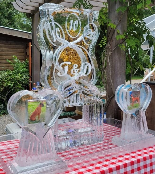 Clear ice sculpture display with heart shapes and plaques on a red-and-white checkered table outdoors