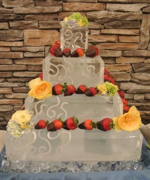 Three-tiered white cake with strawberries and flowers against a stone wall
