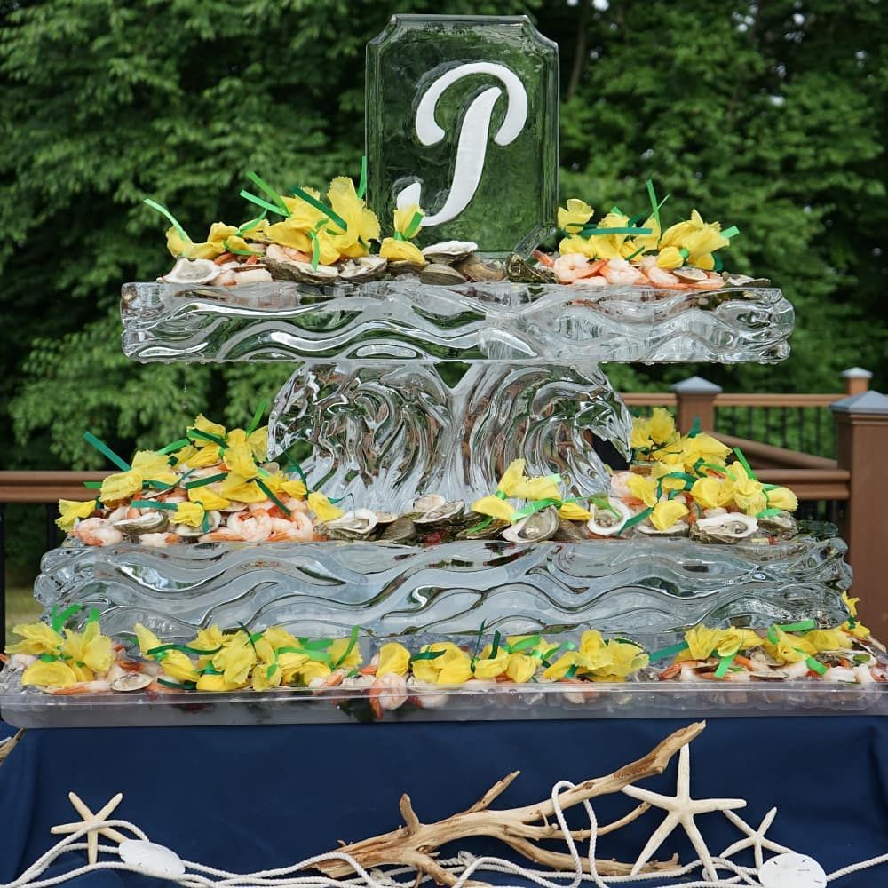 Layered glass fountain sculpture with yellow flowers and a white monogram on top outdoors