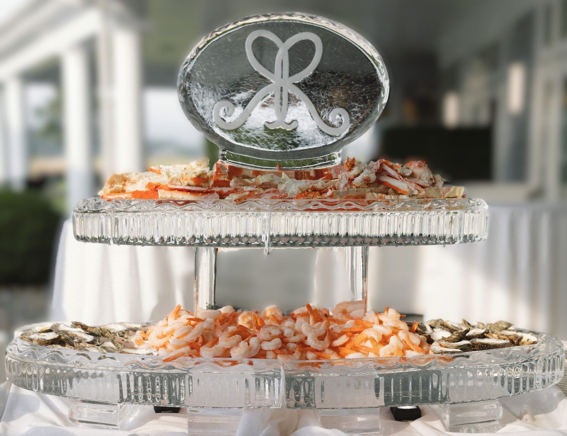 Two-tier crystal buffet stand with orange and white appetizers and a silver monogram topper