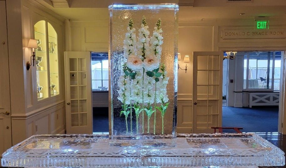 Elegant white floral display in a clear glass enclosure on a mirrored pedestal in a gallery-like room
