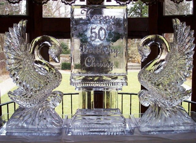 Two glass swans flanking a silver 50th anniversary plaque on a table