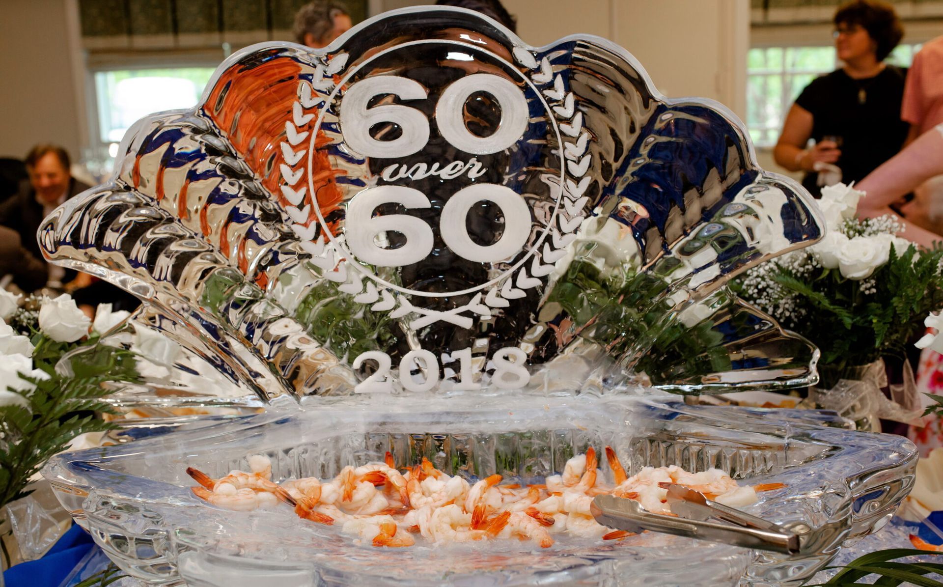 Ice sculpture centerpiece with “60 60” on top, surrounded by flowers and shrimp on a banquet table
