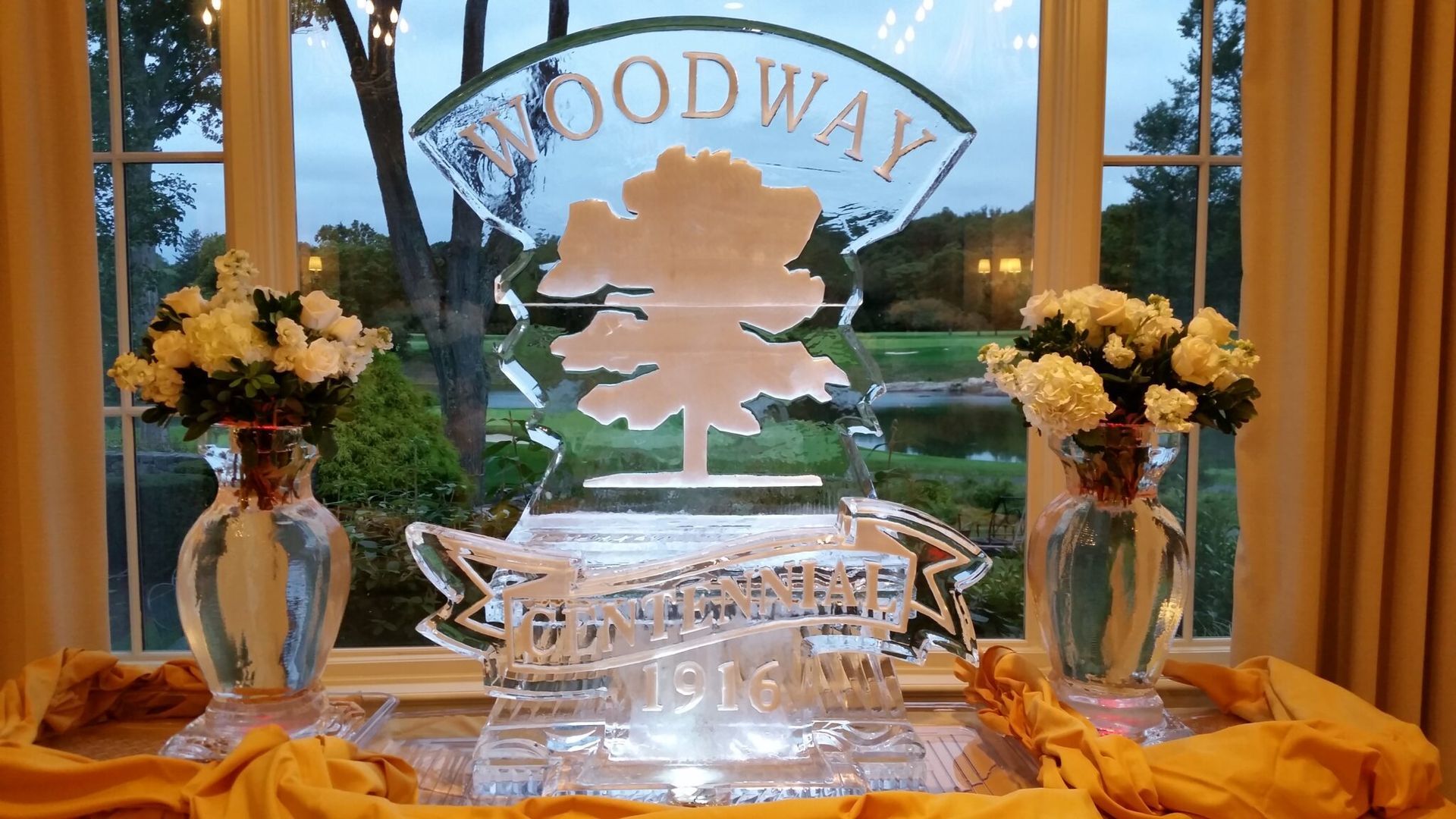 Elegant window display with white floral arrangements, crystal decor, and a “WOODWAY” sign at sunset