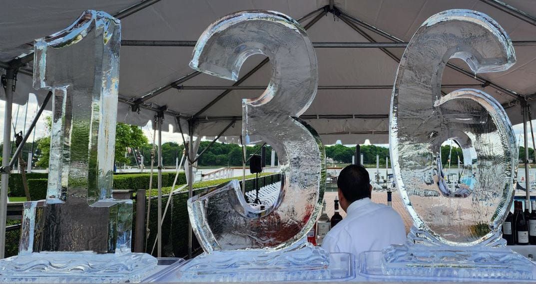 Large ice sculpture numbers “136” with a person standing in front under a canopy outdoors