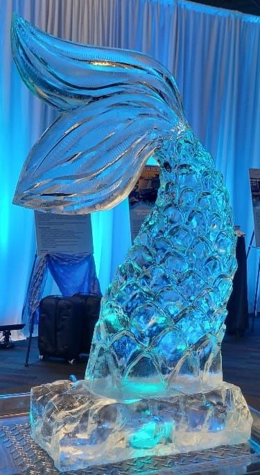 Blue-lit abstract mermaid tail sculpture on an ice-like base in a draped event display