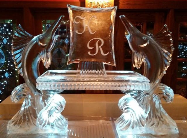 Ornate ice sculpture with two dolphins flanking a pedestal engraved with “JR”