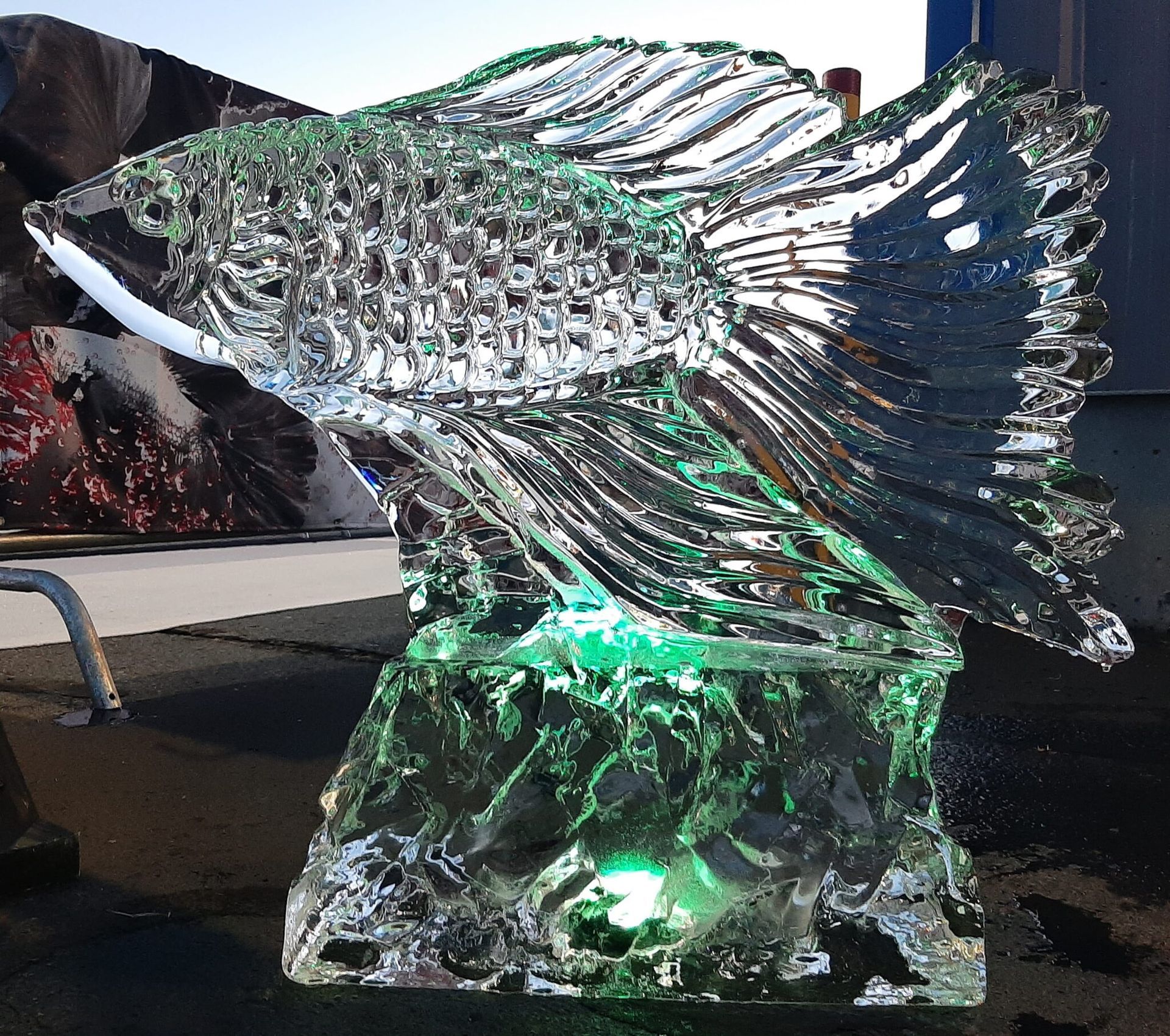 Glass fish sculpture on a pedestal, with clear and green highlights, displayed indoors.