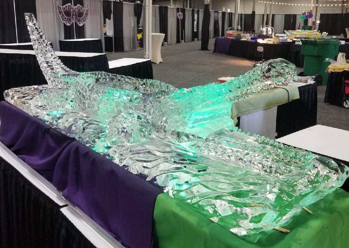 Large translucent glass alligator sculpture displayed on a purple-draped table in an exhibition hall