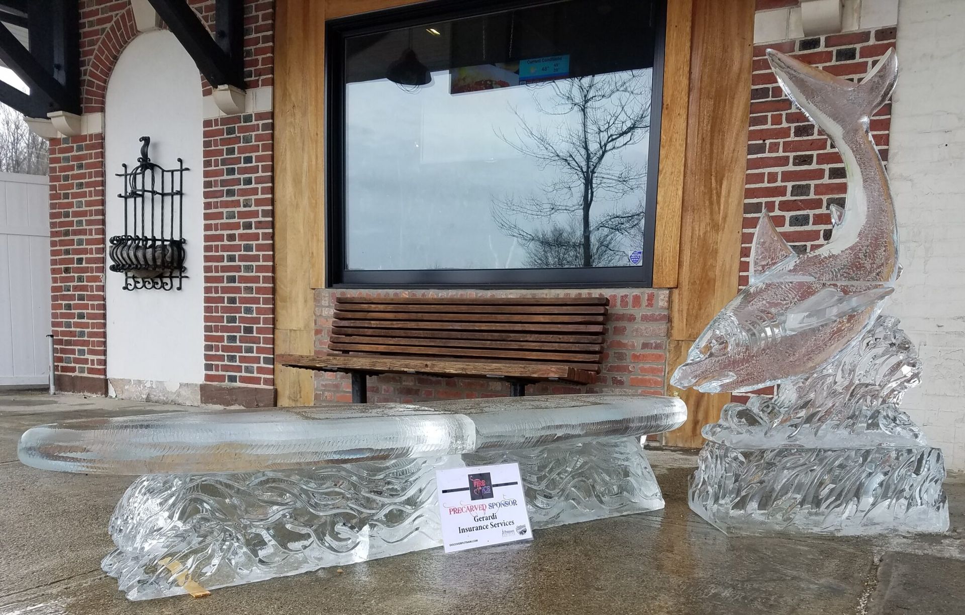 Clear ice sculptures on wet pavement in front of a brick storefront and bench