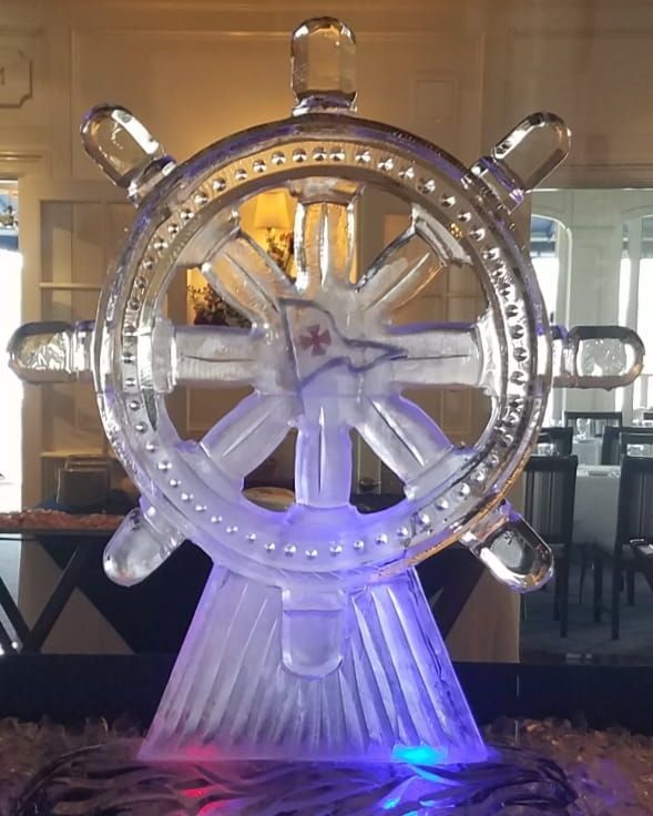Large illuminated ship’s wheel sculpture glowing blue and white indoors on a pedestal