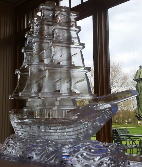 Clear glass sailboat sculpture on a table by large windows