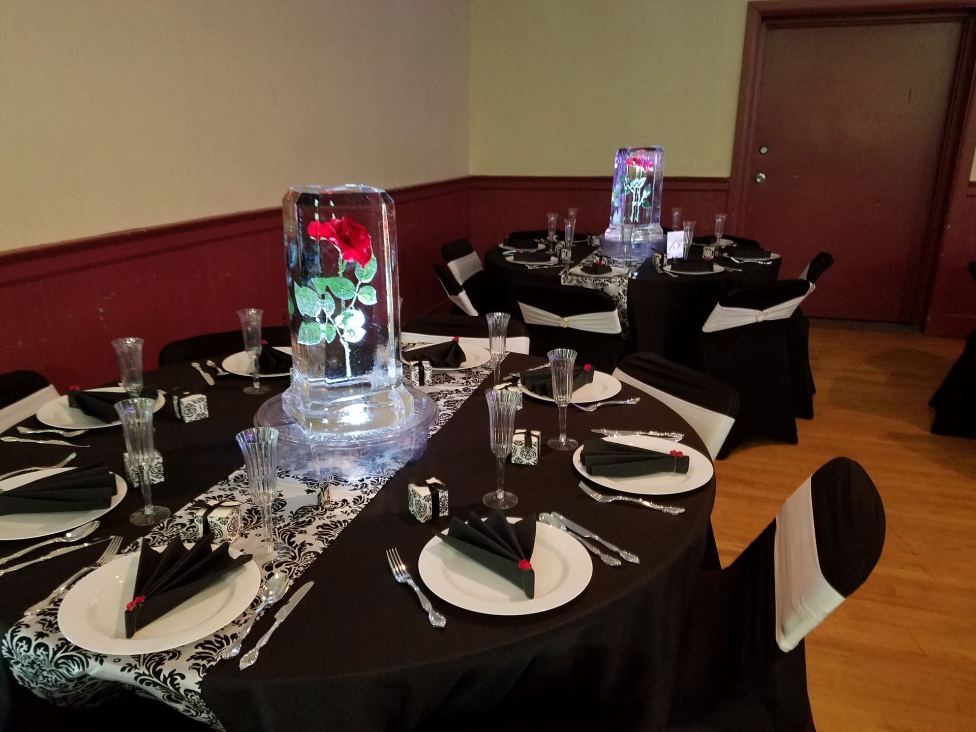 Round banquet tables set for a formal dinner in a dimly lit room with red walls and floral centerpieces