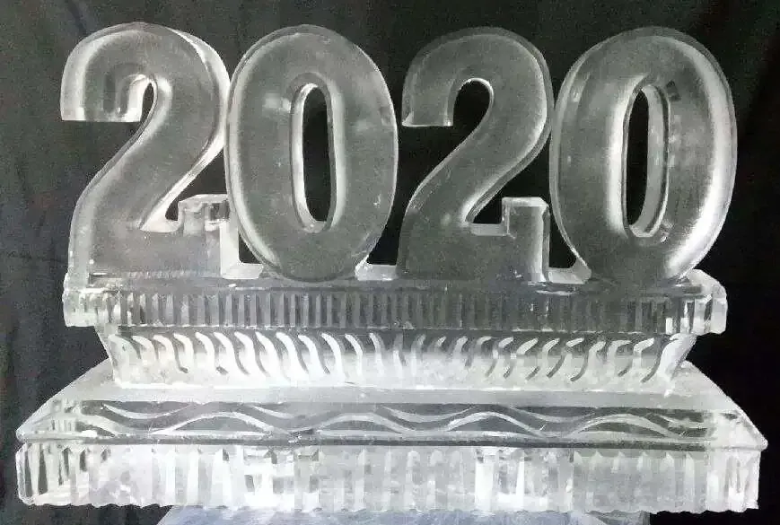 Clear ice sculpture of “2020” on a carved base against a dark background