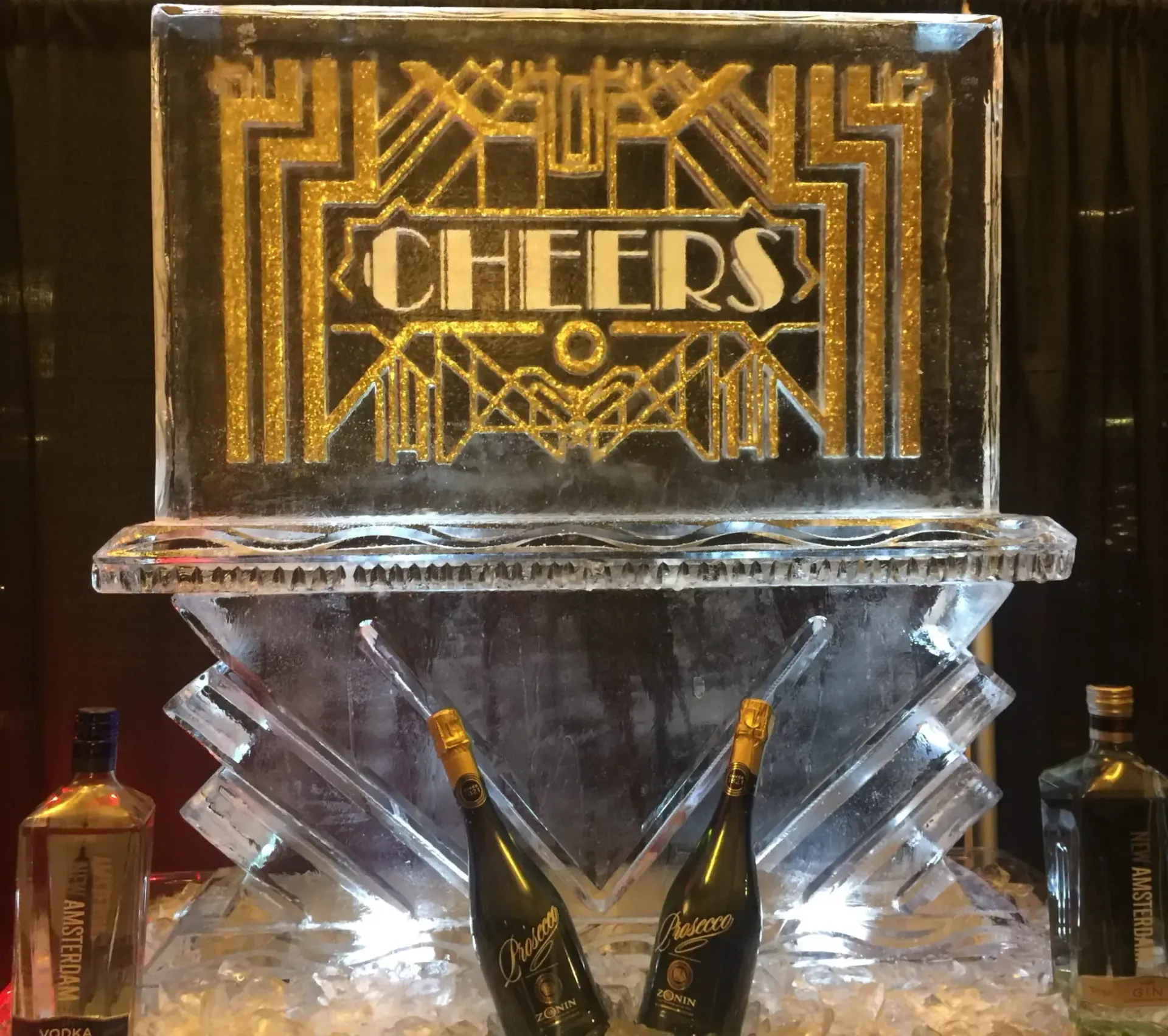 Ice sculpture with gold “CHEERS” sign and champagne bottles at a dimly lit event display