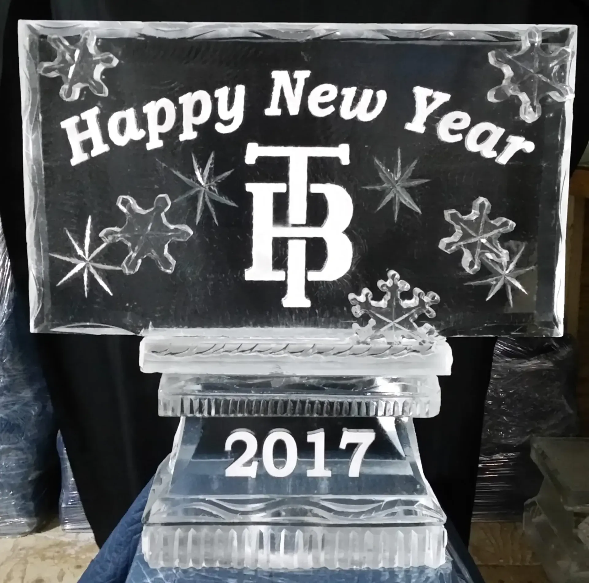 Clear ice sculpture with “Happy New Year,” “2017,” and TP logo against a dark background