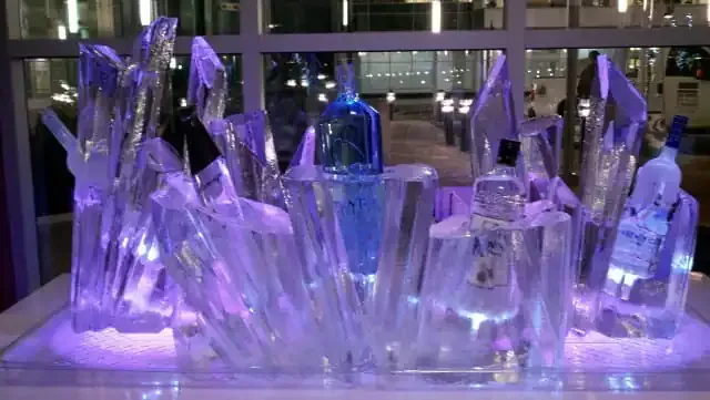 Purple-lit ice sculpture display with carved crystal-like forms on a table indoors