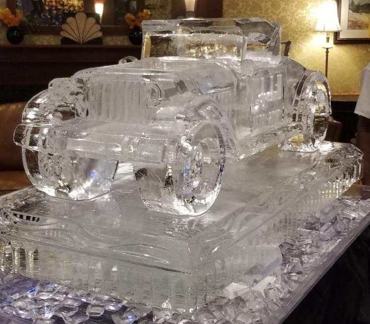 Clear glass sculpture of a vintage car on a table, lit warmly indoors