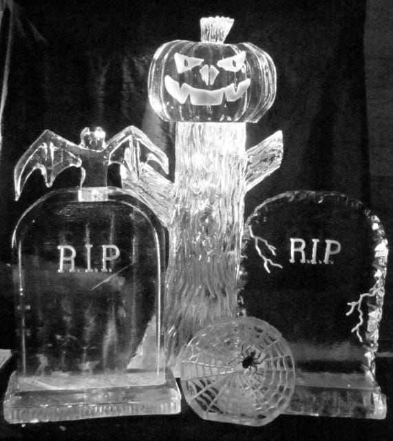 Halloween gravestone display with jack-o'-lantern, bat, and spider web accents under black backdrop