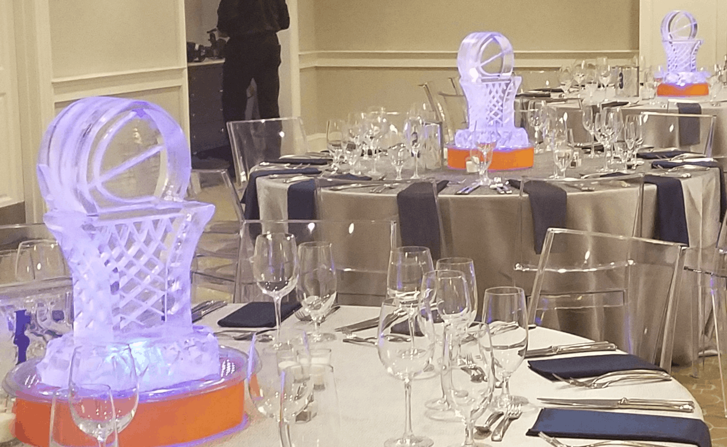 Crystal ice sculpture centerpiece on a banquet table with glassware and purple lighting