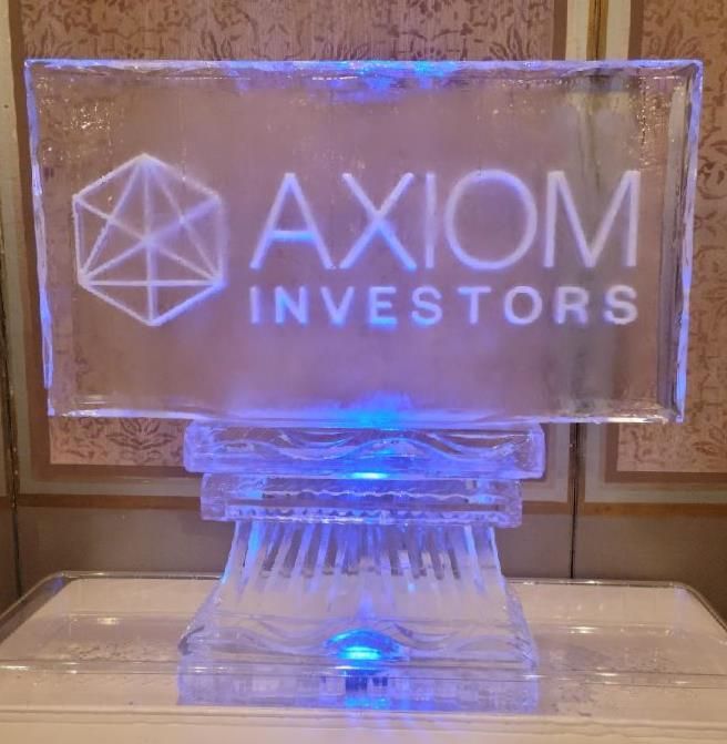 Clear acrylic sign lit blue reading “AXIOM INVESTORS” on a decorative stand.