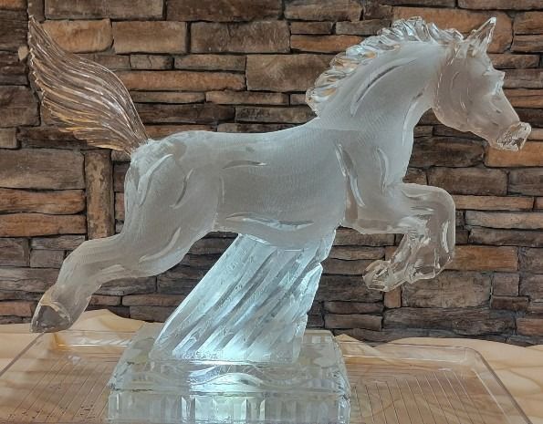 Clear glass Pegasus sculpture on a stone pedestal against a stacked stone wall.