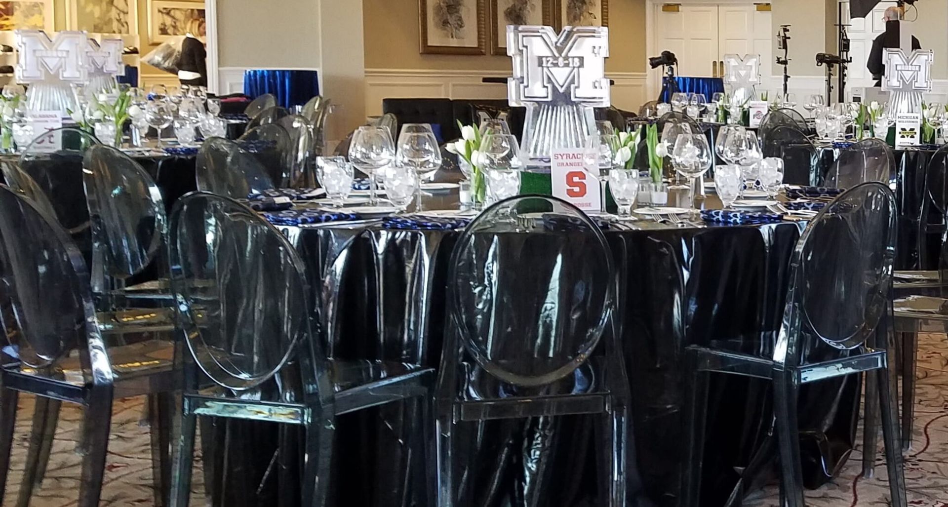 Banquet table with black tablecloth and clear chairs in a decorated event hall, table number 5 displayed