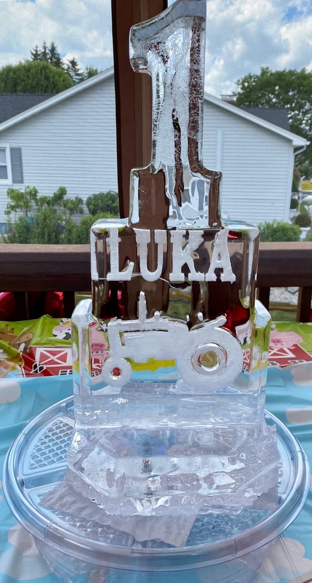 Clear ice sculpture cake with “LUKA” and a large 1 on a table outdoors