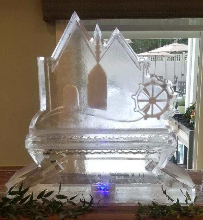 Transparent ice sculpture of a church with a cross-like wheel, lit with a blue glow on a table