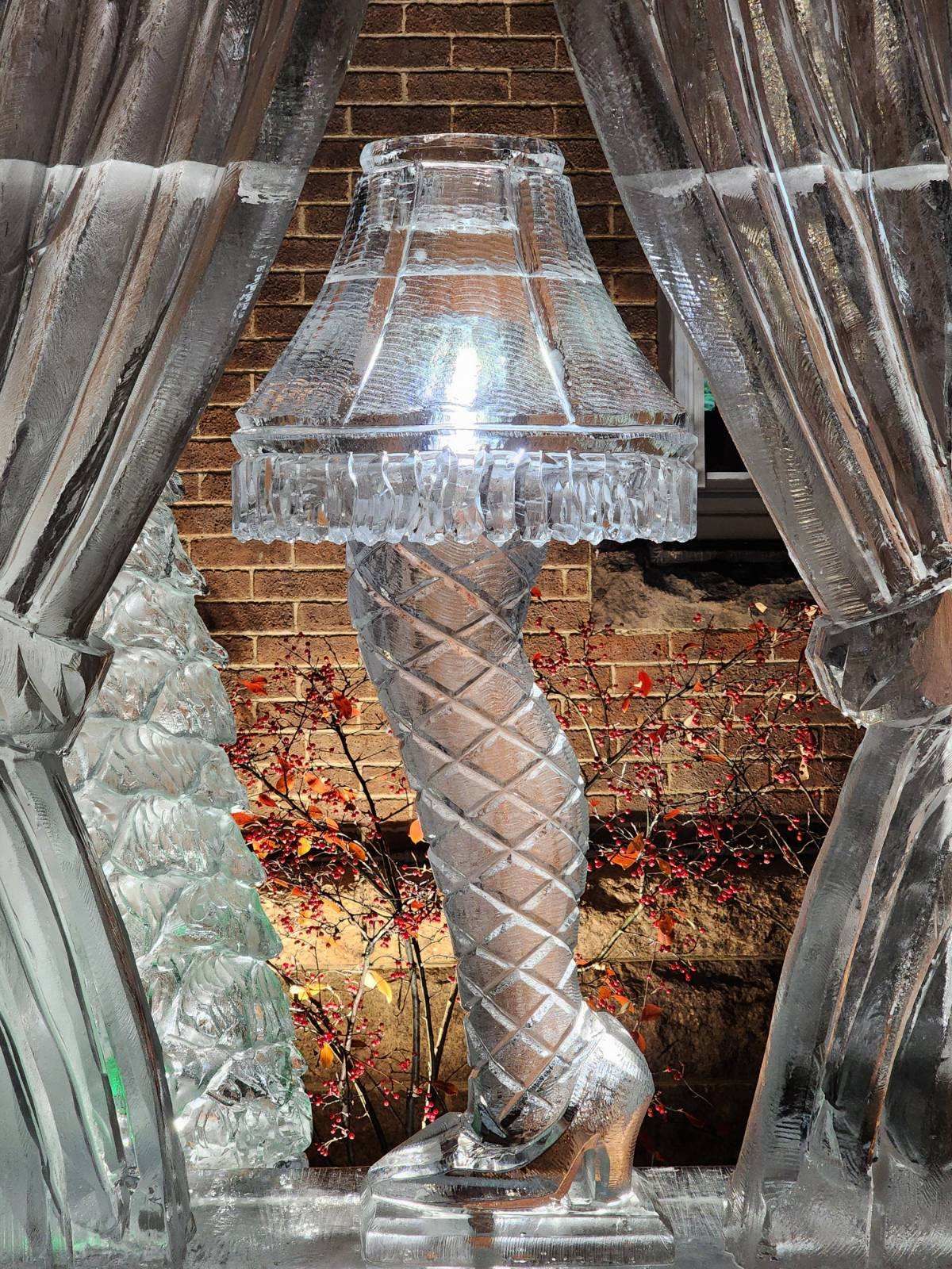 Metallic lamp with pleated shade and twisted base framed by gray curtains against a brick wall.