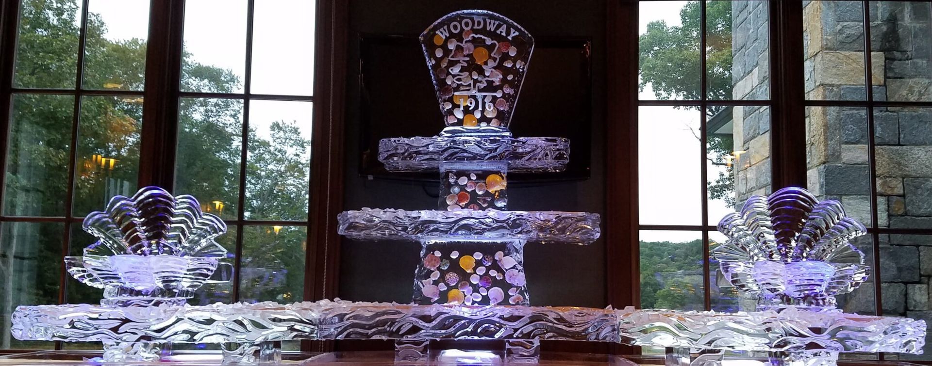 Three-tier crystal fountain with water flowing, lit indoors in front of large windows