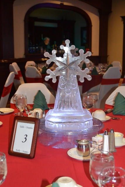 Snowflake-shaped ice sculpture on a red banquet table with place settings and a table number sign.