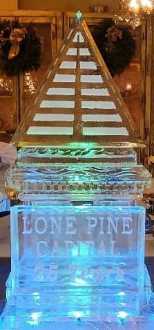 Ice sculpture with a pine tree and the words “Lone Pine Capital” lit in blue and green at night