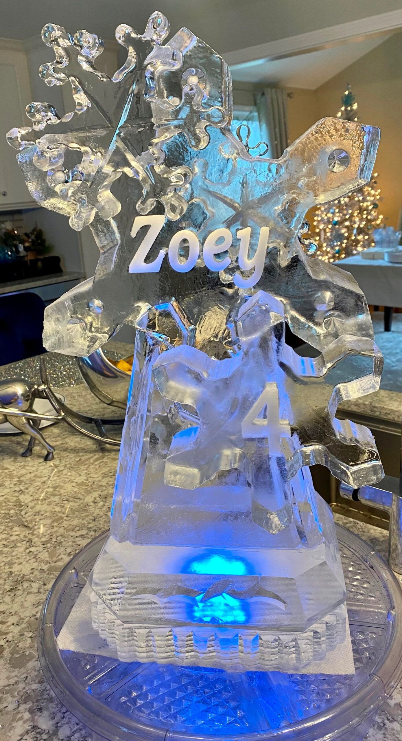 Ice sculpture with “Zoey” and “54” glowing blue on a decorated table at an event