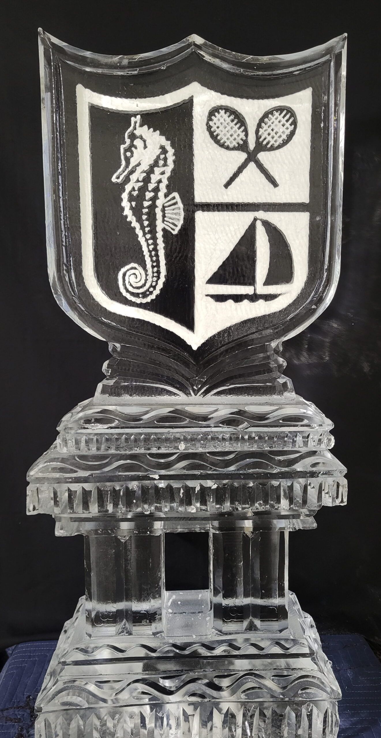 Silver trophy with shield emblem featuring tennis rackets and sailboat on a pedestal base