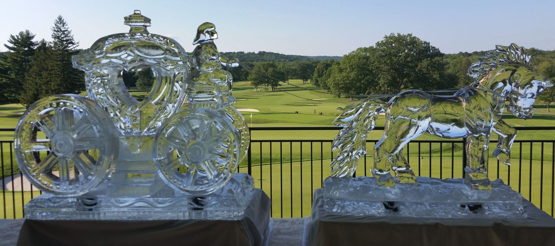 Two clear glass sculptures on a table overlooking a green lawn and trees under a blue sky